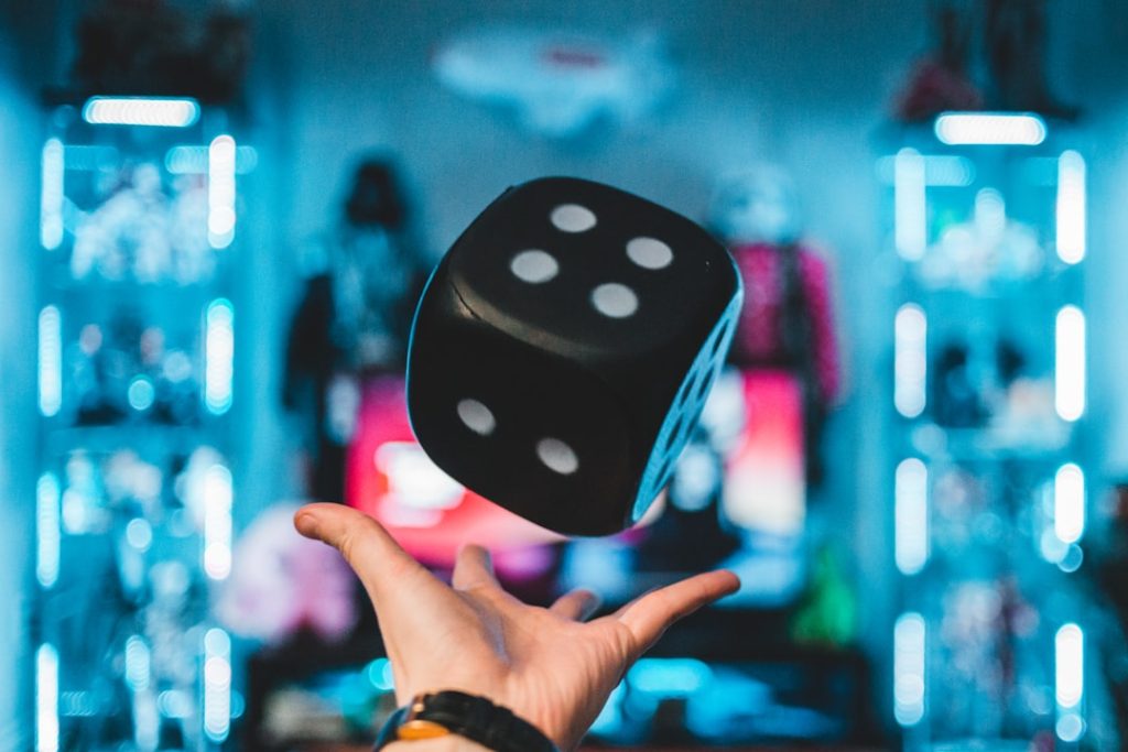 A black die floating above a hand in a neon-lit casino environment, representing Stake dice game automation. Photo by Kaysha on Unsplash.