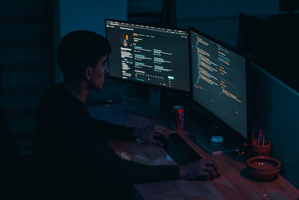 photo-1623479322729-28b25c16b011jpg - StakeProSoft Developer working at dual monitor dark workstation running automated bot scripts