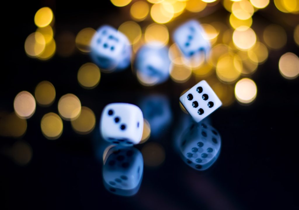 photo-1627744842997-81622949c9f4jpg - StakeProSoft White dice rolling in mid-air against bokeh casino lights, illustrating dice gambling strategy